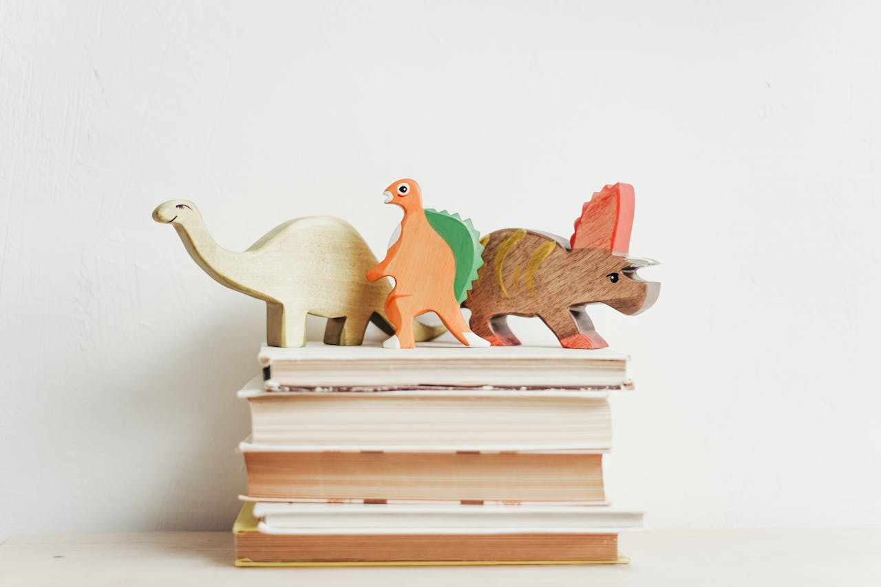about-02 Colorful wooden dinosaurs on top of a stack of hardcover books on a light background.