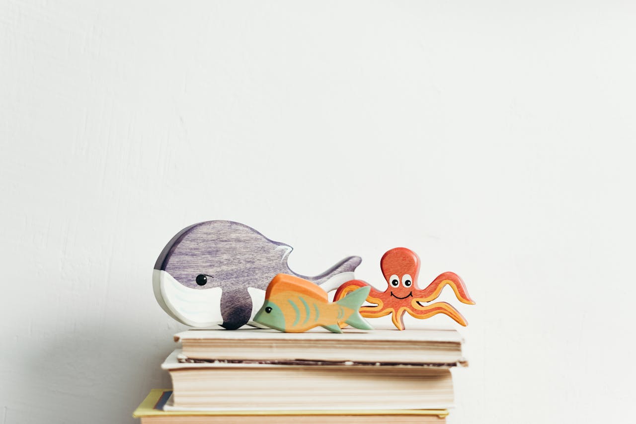 services-img Charming wooden toys of marine animals on stacked books with a white background, perfect for kids' decor.